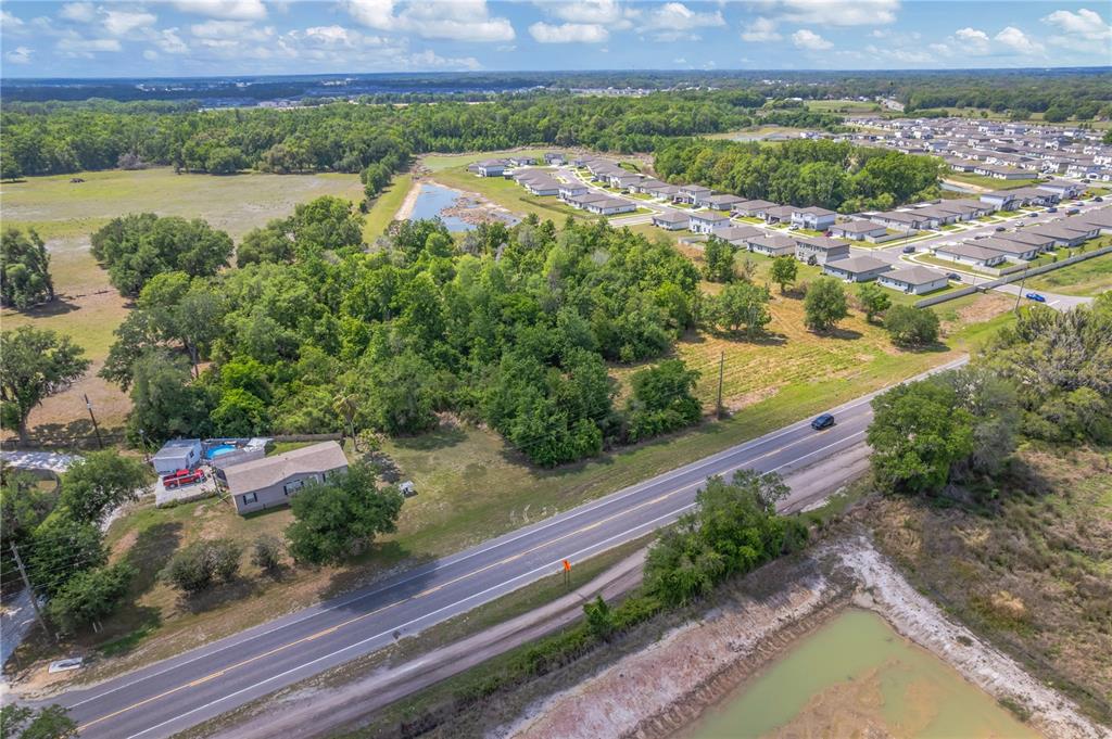 An aerial view shows a house with a pool next to a road and woods — CORNER OF PAUL S BUCHMAN HWY & FORREST PLUM CT, ZEPHYRHILLS, FL