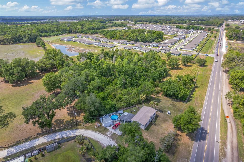 An aerial view shows a house with a pool next to a road and woods — CORNER OF PAUL S BUCHMAN HWY & FORREST PLUM CT, ZEPHYRHILLS, FL