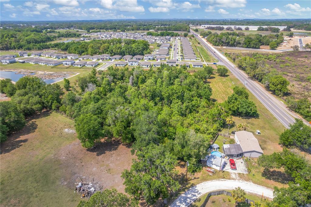 An aerial view shows a wooded lot adjacent to a residential neighborhood and a road — CORNER OF PAUL S BUCHMAN HWY & FORREST PLUM CT, ZEPHYRHILLS, FL
