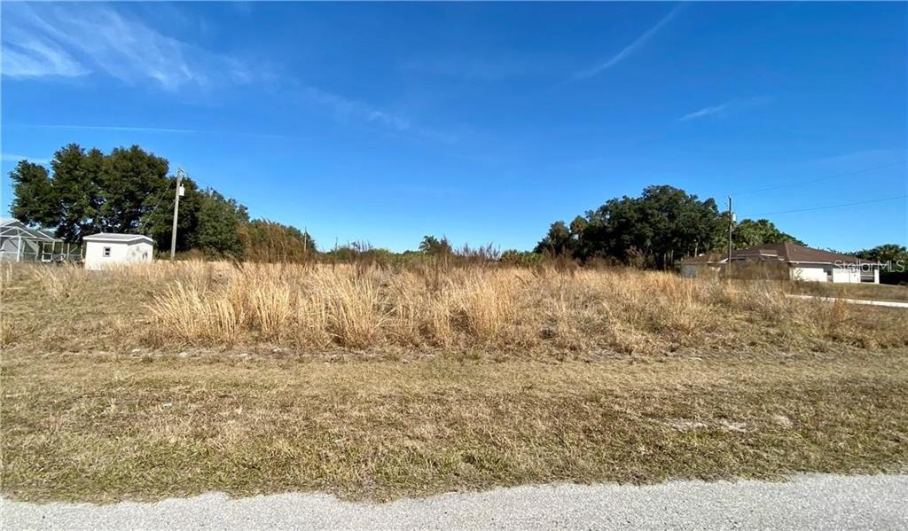 A vacant, grassy lot with tall weeds sits under a clear blue sky — 165 WALDO STREET, PORT CHARLOTTE, FL