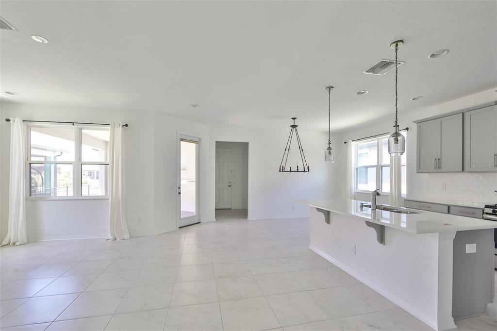 A bright, open-concept kitchen and living area features white tile flooring and gray cabinetry — 3044 ABRAMS TRAIL, ODESSA, FL