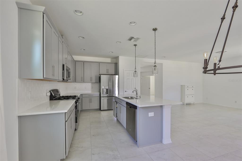 A modern kitchen features gray cabinets, white countertops, a central island, and stainless steel appliances — 3044 ABRAMS TRAIL, ODESSA, FL