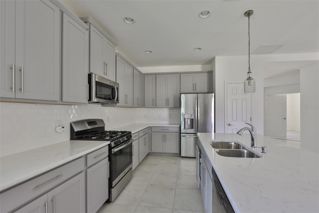 A modern kitchen features gray cabinets, white countertops, stainless steel appliances, and a kitchen island — 3044 ABRAMS TRAIL, ODESSA, FL