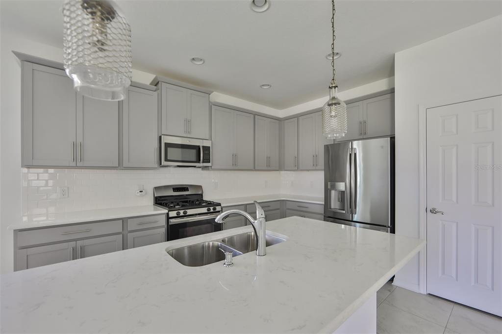 A kitchen features gray cabinets, white countertops, stainless steel appliances, and a central island sink — 3044 ABRAMS TRAIL, ODESSA, FL