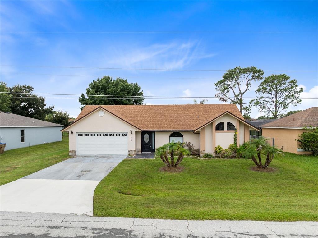 A single-story house with a tan stucco exterior, a brown shingled roof, and a two-car garage — 1025 DERBYSHIRE DRIVE, KISSIMMEE, FL