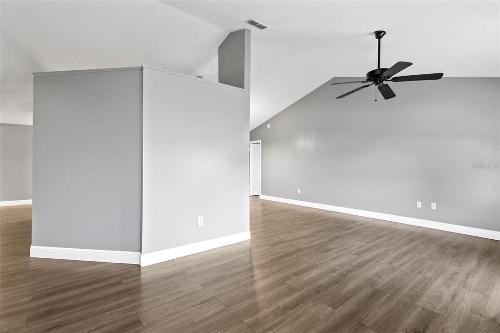 A living room features light gray walls, wood-look flooring, and a vaulted ceiling with a fan — 1025 DERBYSHIRE DRIVE, KISSIMMEE, FL