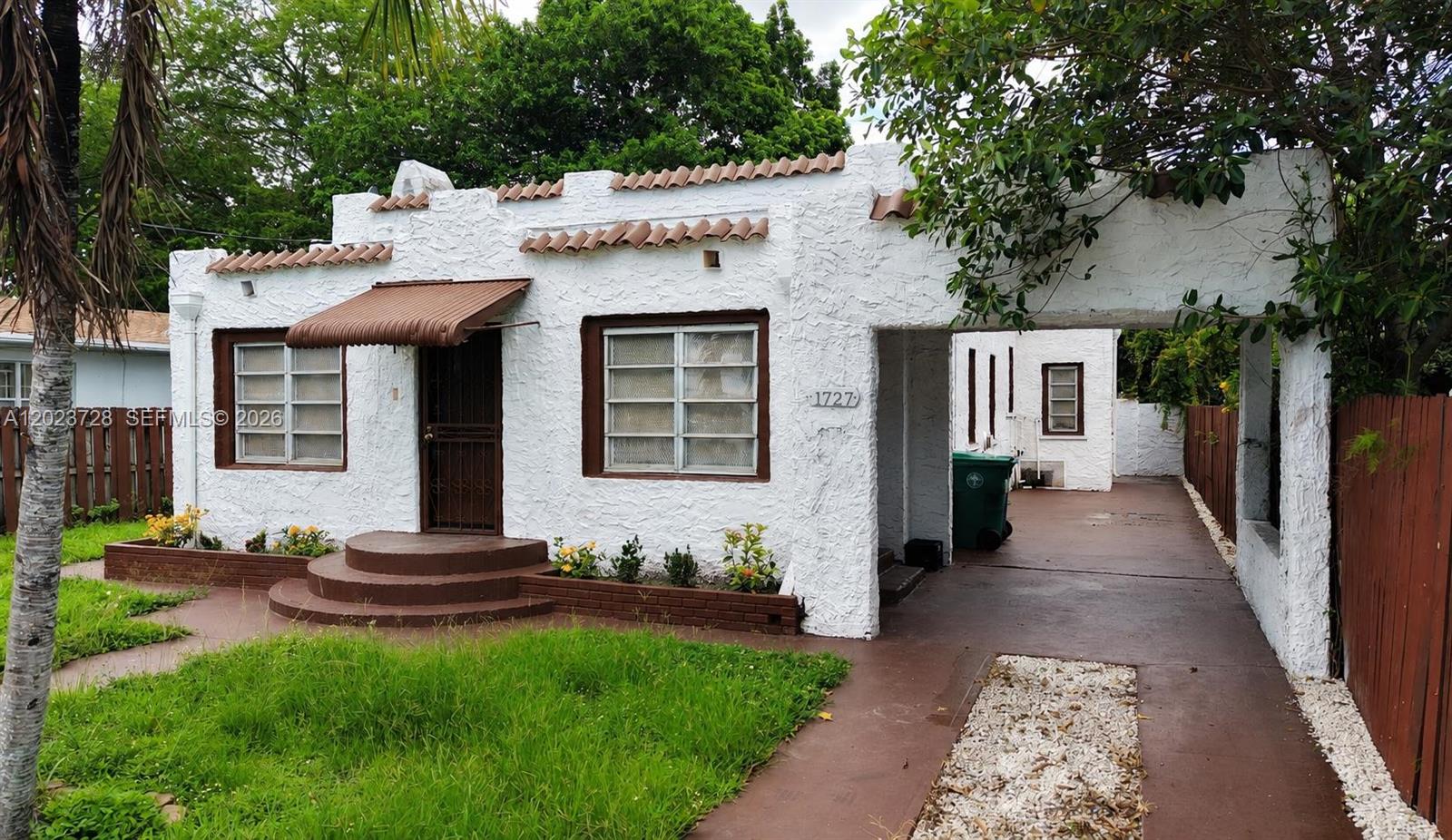 A white stucco house with a brown awning, tiled roof accents, and a side carport — 1727 NW 50th St, Miami FL 33142, MIAMI, FL