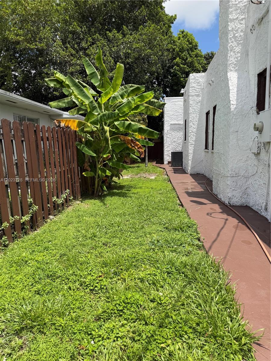 A narrow grassy side yard sits between a wooden fence and a white stucco building — 1727 NW 50th St, Miami FL 33142, MIAMI, FL