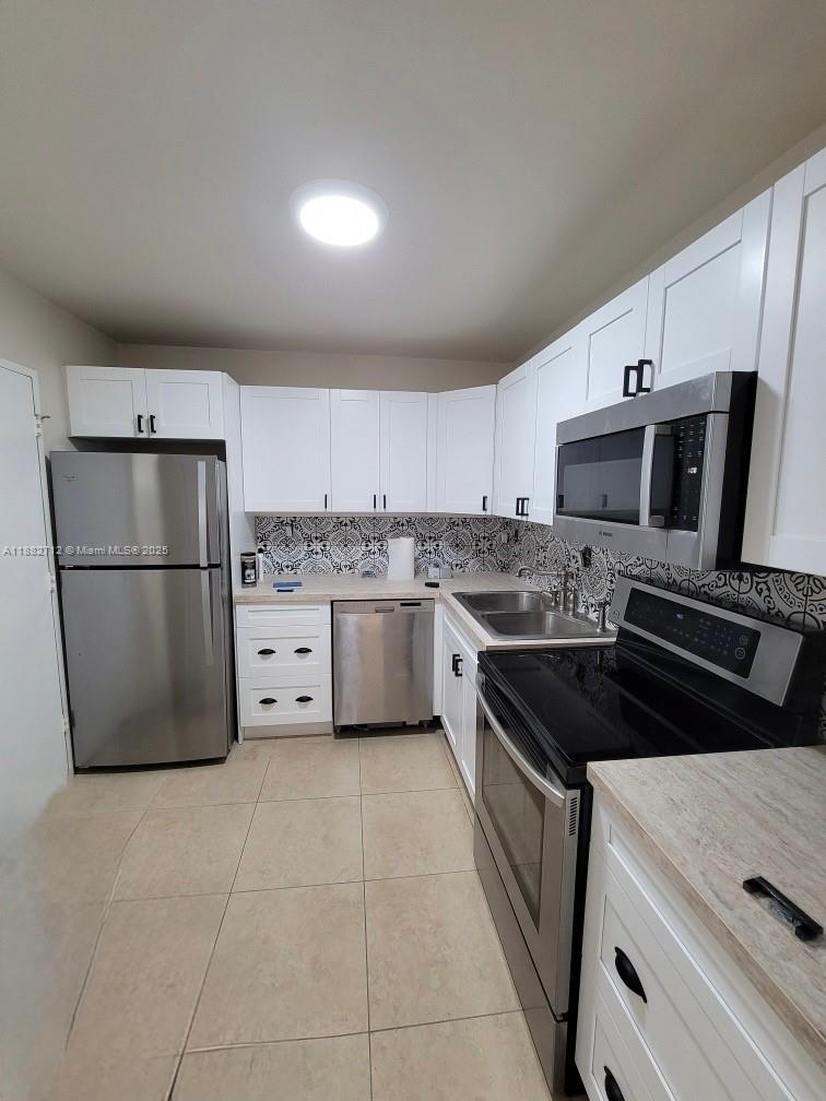 A kitchen features white cabinetry, stainless steel appliances, and a patterned tile backsplash — 500 Three Islands Blvd # 226, Hallandale Beach FL 33009, HALLANDALE BEACH, FL