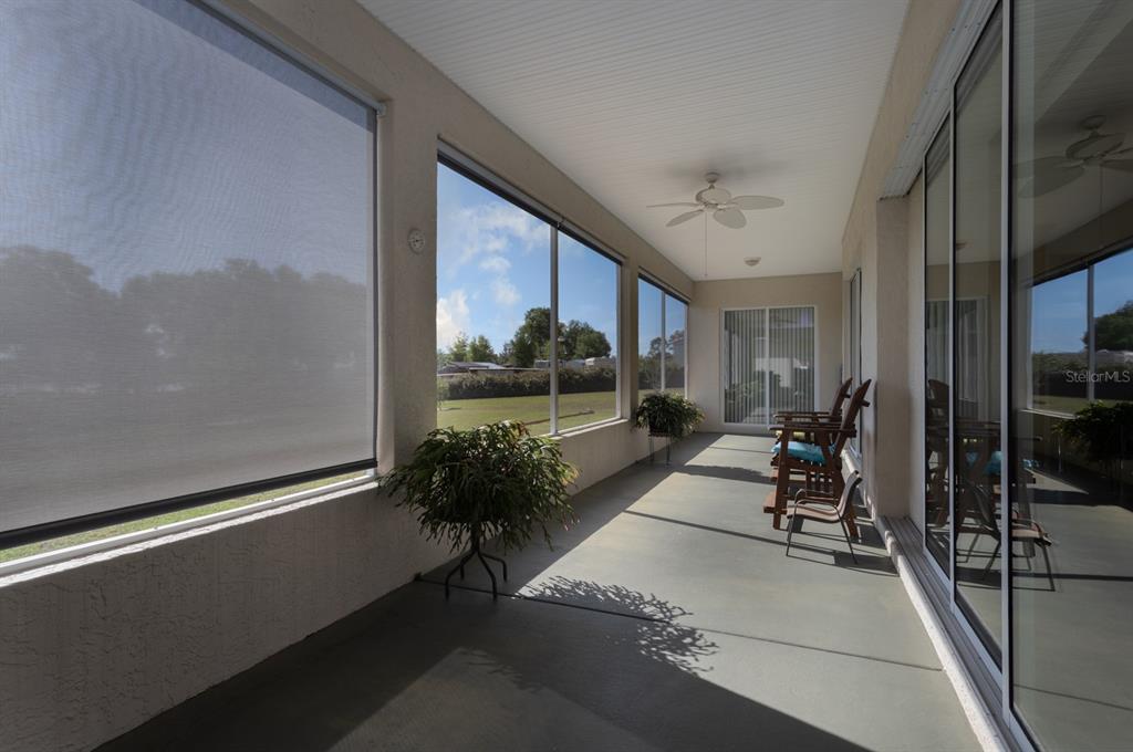 A covered patio features a concrete floor, ceiling fan, large windows, and sliding glass doors — 11395 SE 108TH TERRACE ROAD, BELLEVIEW, FL