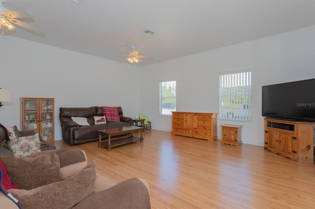 A living room features light wood flooring, a brown leather sofa, and a television console — 11395 SE 108TH TERRACE ROAD, BELLEVIEW, FL