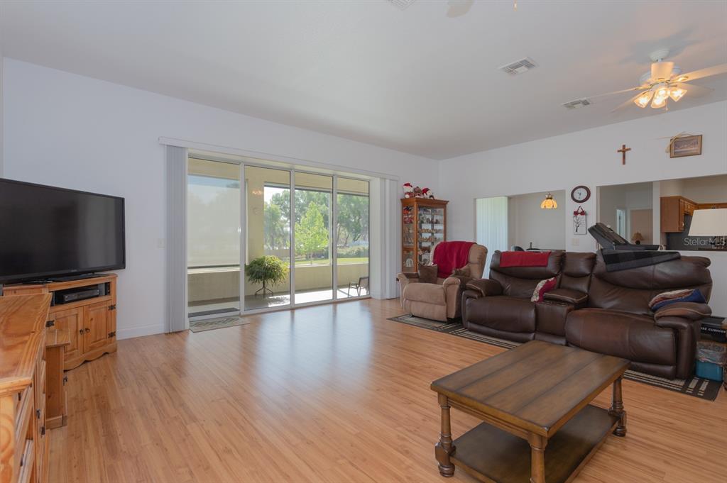 A living room with wood-look flooring, a brown leather sofa, and large sliding glass doors — 11395 SE 108TH TERRACE ROAD, BELLEVIEW, FL