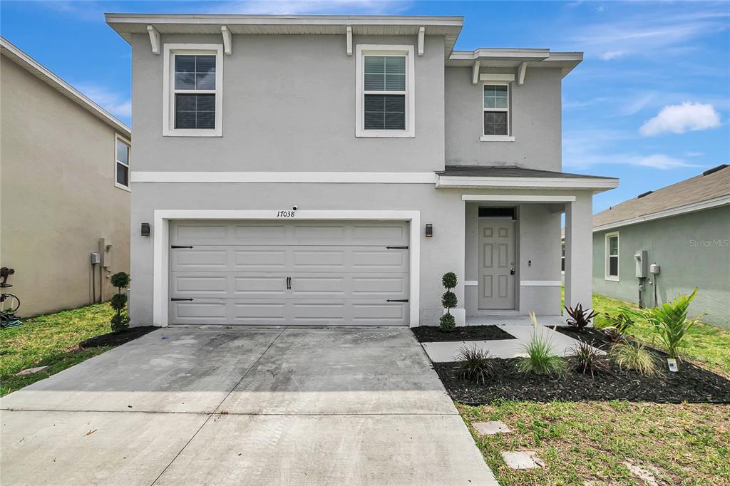 A two-story gray house features a two-car garage, a front entrance, and a small yard — 17038 WAVE TRESSLE PLACE, WIMAUMA, FL