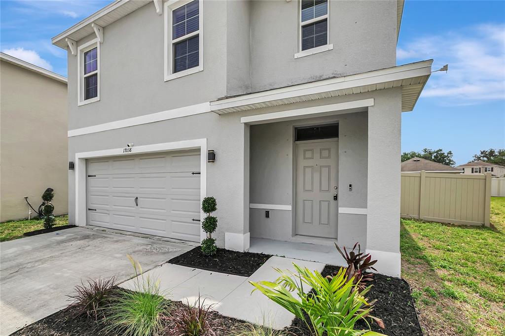A two-story gray house features a single-car garage, a front entryway, and landscaped garden beds — 17038 WAVE TRESSLE PLACE, WIMAUMA, FL