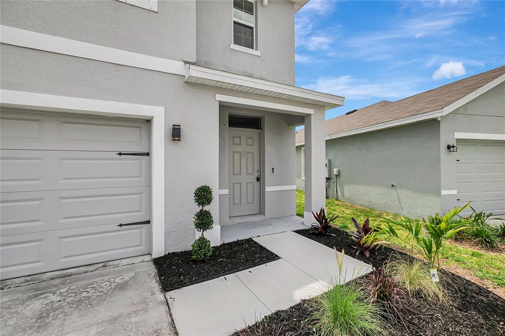 The exterior of a two-story house features a gray garage, a front door, and landscaping — 17038 WAVE TRESSLE PLACE, WIMAUMA, FL