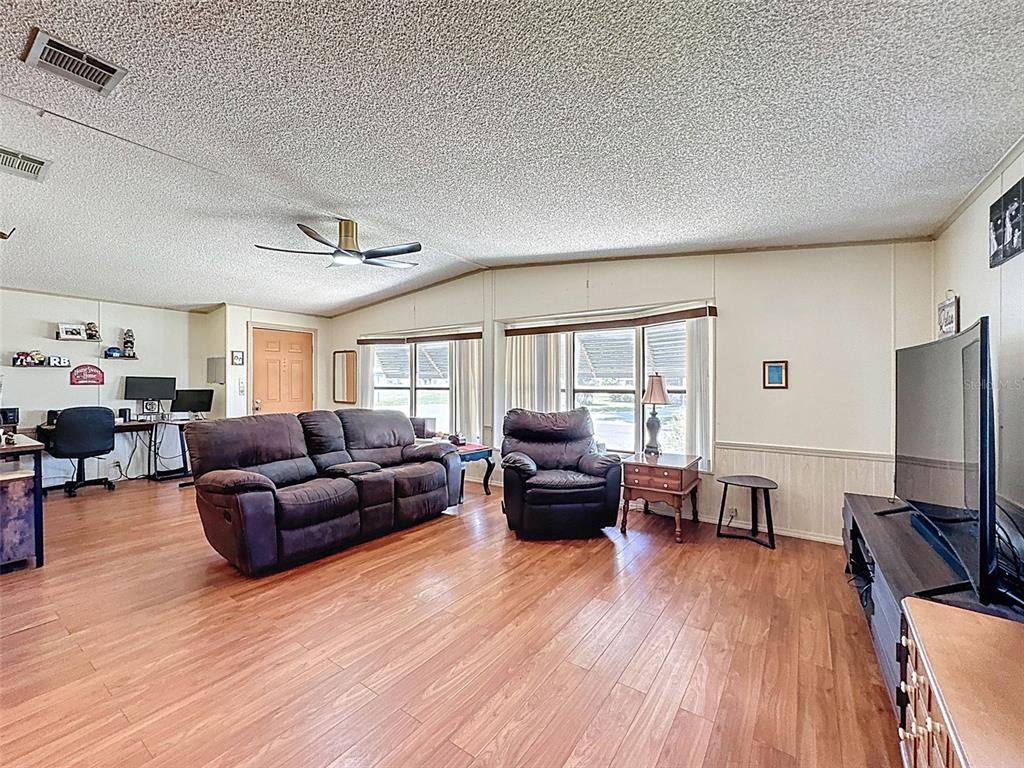 A living room with wood-look flooring, a ceiling fan, a brown sofa, and a television — 4202 ORCHID BOULEVARD, LAKE WALES, FL