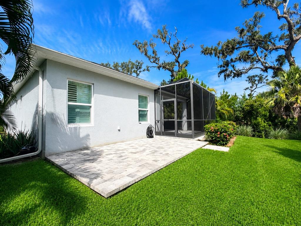 A light-colored house exterior features a paved patio and a screened-in porch in the backyard — 10806 PINE BLUFF GLEN, PARRISH, FL
