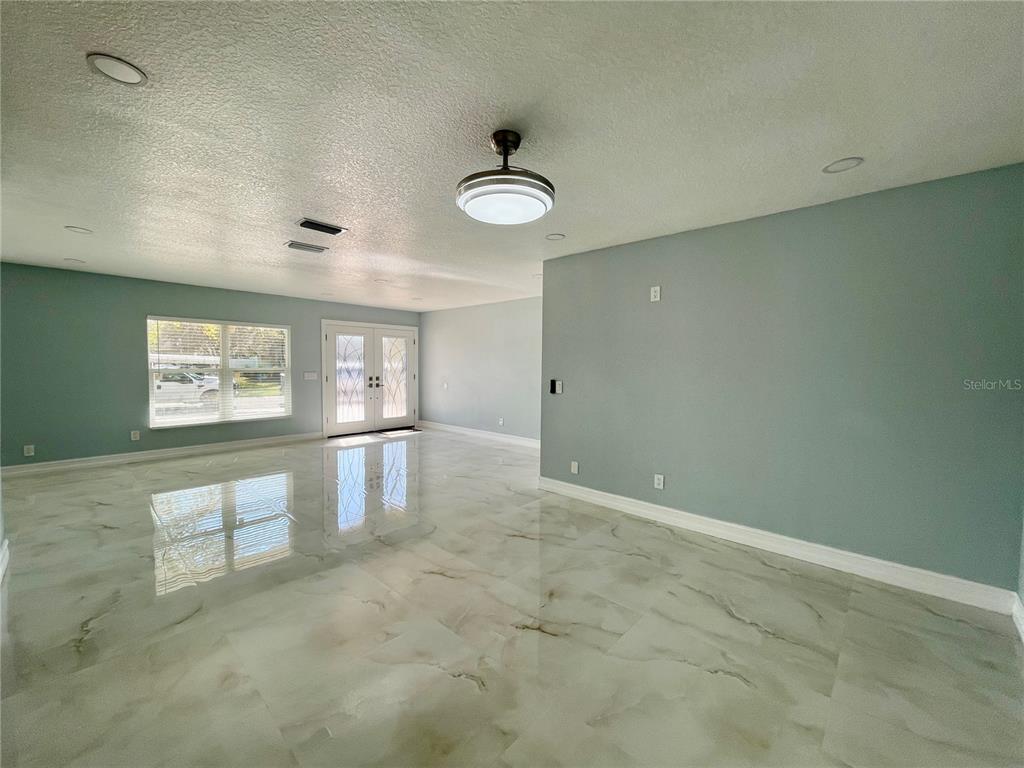 A bright, empty room features light blue walls, a glossy marble floor, and double doors — 8503 WOODWICK COURT, TAMPA, FL