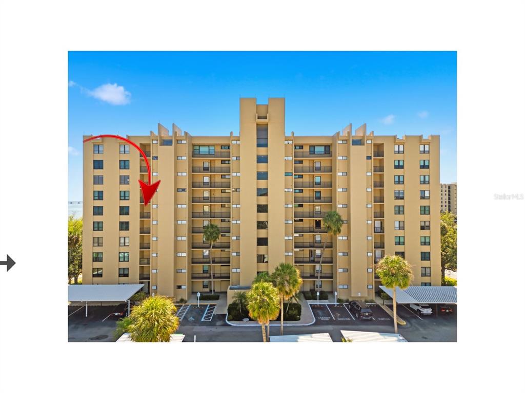 An exterior view of a multi-story tan apartment building with a red arrow pointing toward balconies — 2616 COVE CAY DRIVE UNIT 602, CLEARWATER, FL