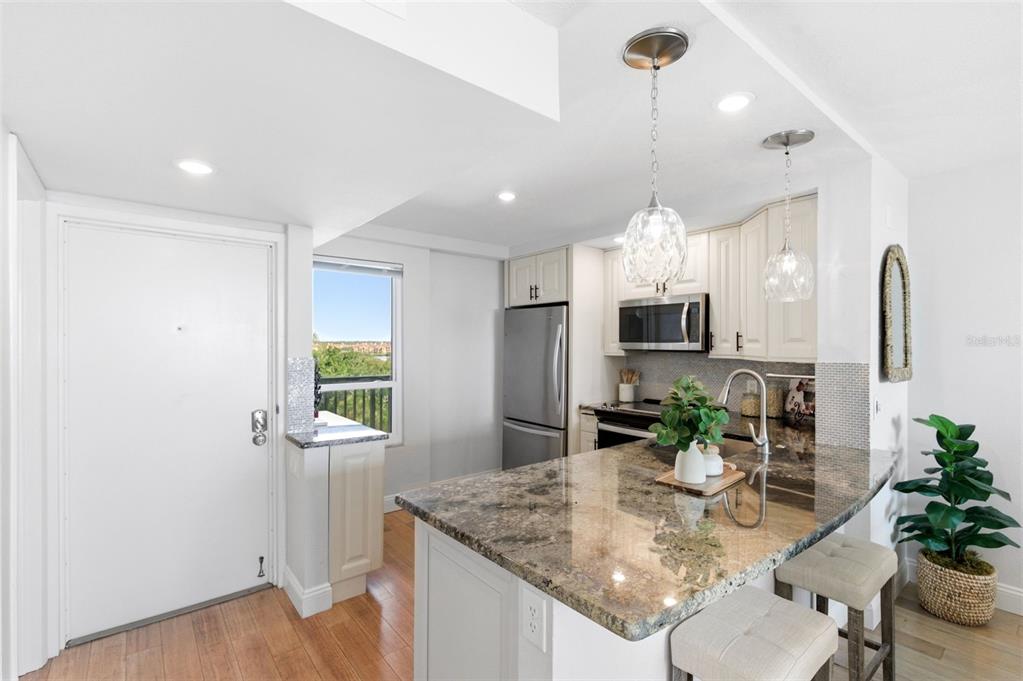 A kitchen features granite countertops, stainless steel appliances, white cabinetry, and a breakfast bar — 2616 COVE CAY DRIVE UNIT 602, CLEARWATER, FL