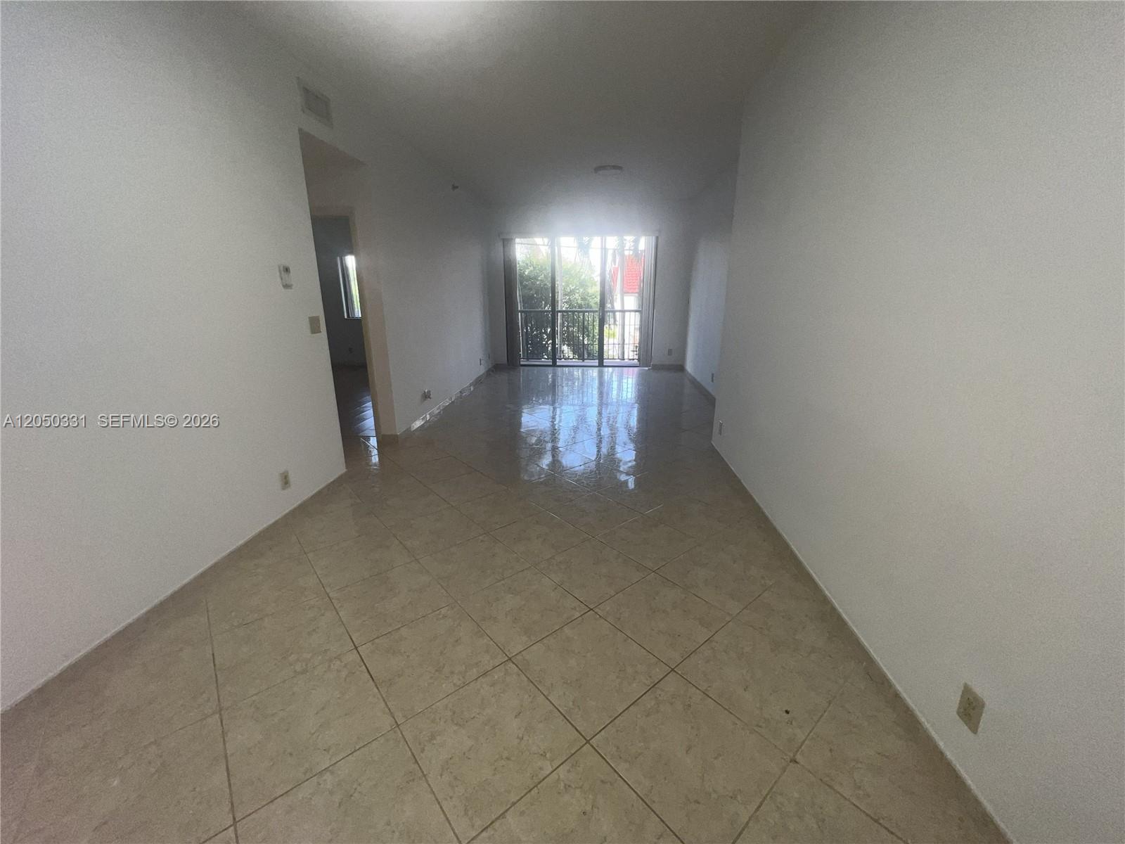An empty living area features light-colored tile flooring, white walls, and a sliding glass door — 8816 Collins Ave # 105, Surfside FL 33154, SURFSIDE, FL