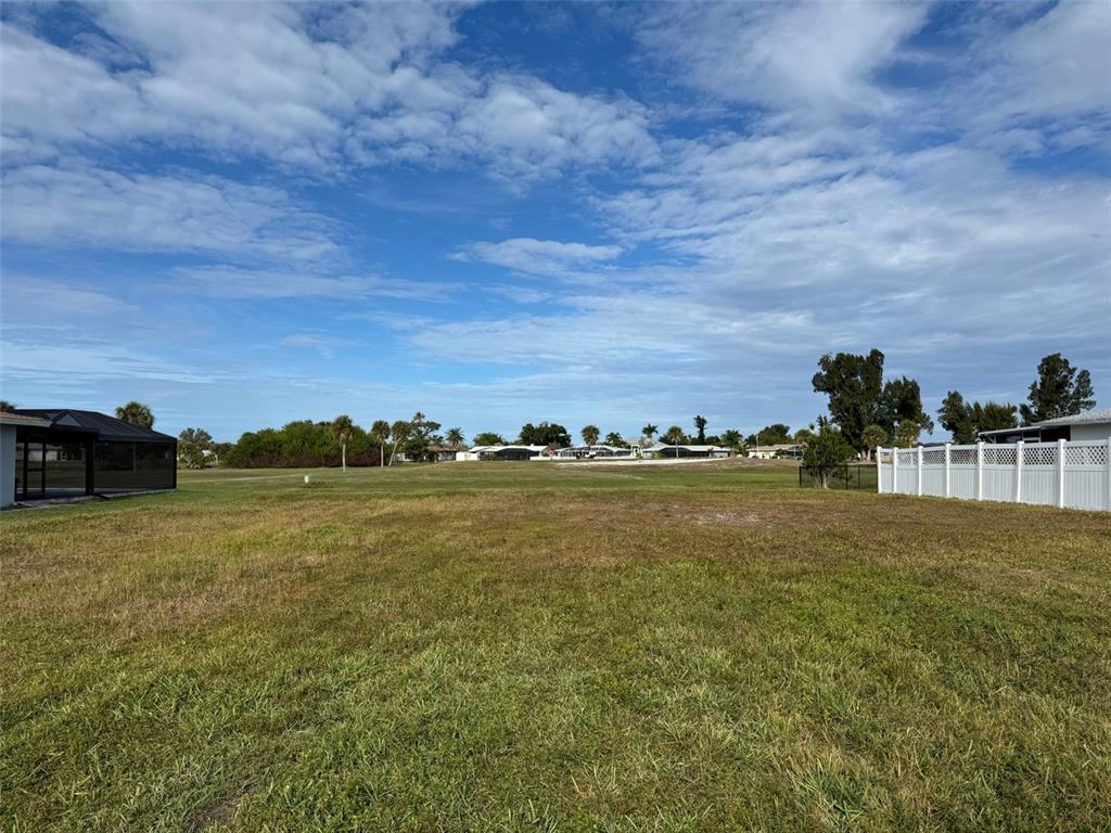 A large, grassy vacant lot is bordered by a white fence and neighboring houses — 48 OAKLAND HILLS COURT, ROTONDA WEST, FL