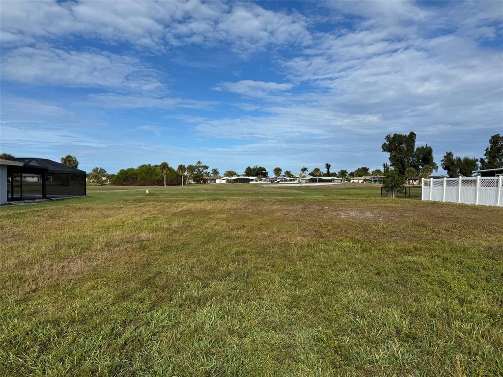 A vacant, grassy lot sits between a screened-in patio and a white vinyl fence — 48 OAKLAND HILLS COURT, ROTONDA WEST, FL
