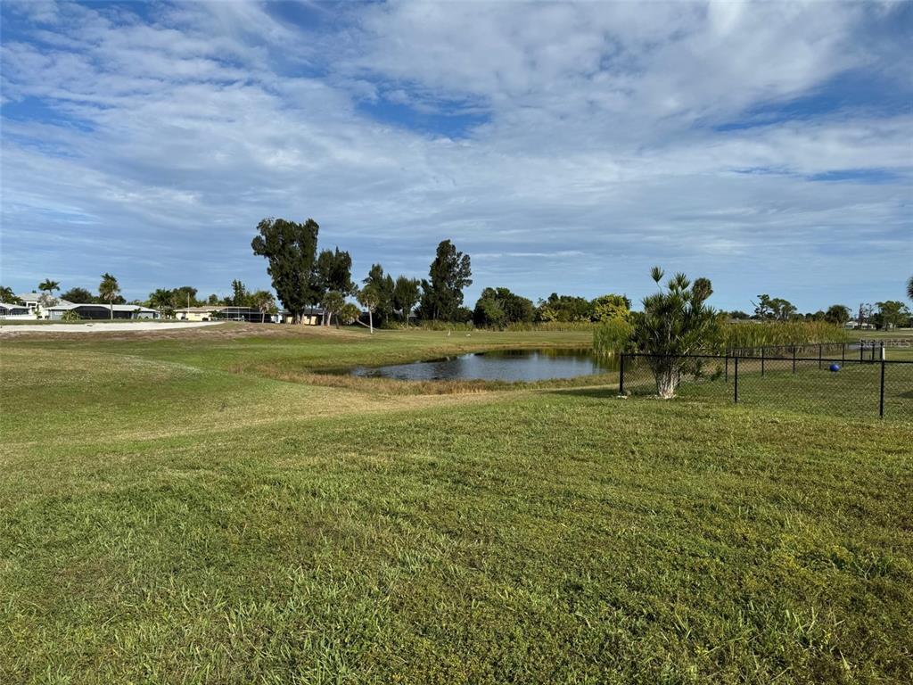A grassy yard overlooks a small pond with a fenced area and distant trees — 48 OAKLAND HILLS COURT, ROTONDA WEST, FL
