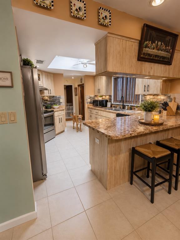 A kitchen features light wood cabinets, granite countertops, tile flooring, and a dog standing inside — 7054 LEXINGTON CIRCLE, BROOKSVILLE, FL