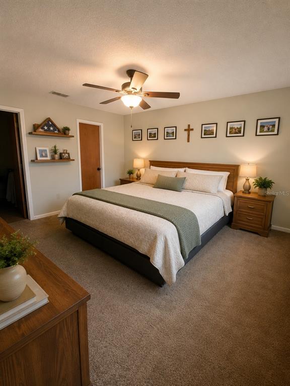 A bedroom features a king-sized bed, wooden nightstands, a ceiling fan, and wall-mounted decor — 7054 LEXINGTON CIRCLE, BROOKSVILLE, FL