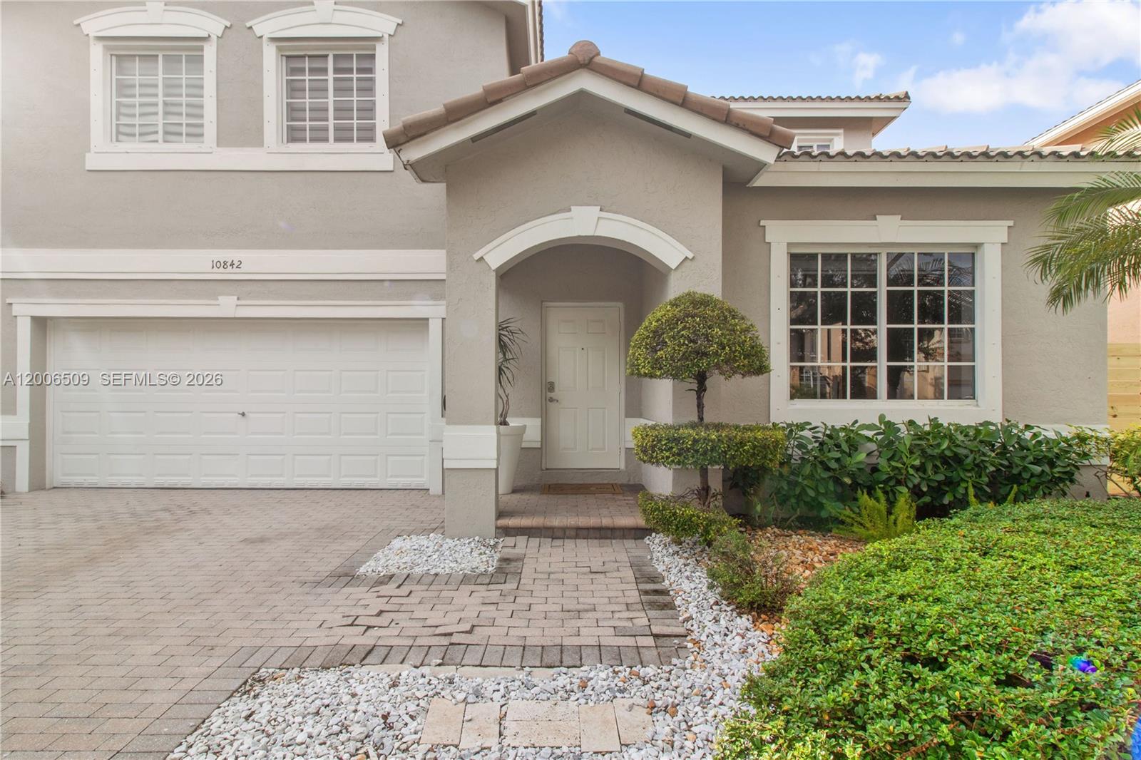 The exterior of a two-story house features a garage, a covered entryway, and landscaped bushes — 10842 NW 53rd Ln, Doral FL 33178, DORAL, FL