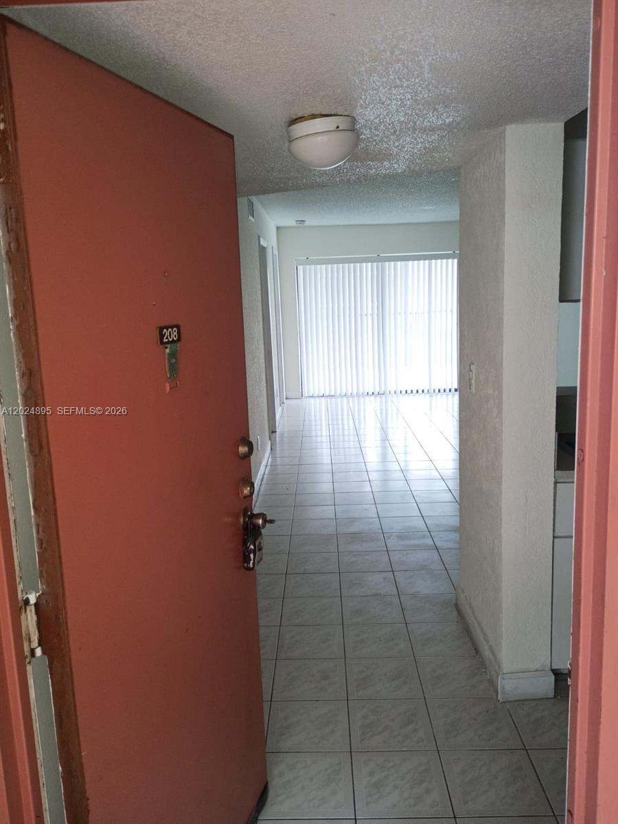 An open door reveals a tiled entryway leading into a bright room with vertical blinds — 3399 Foxcroft Rd # 208, Miramar FL 33025, MIRAMAR, FL