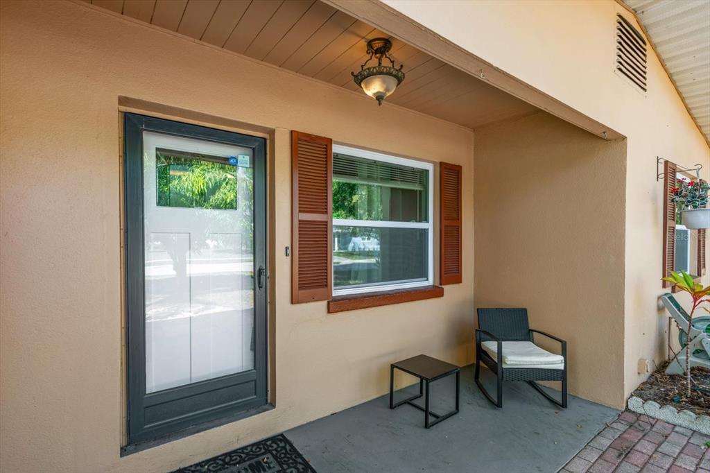 A covered porch features a dark-framed glass door, a window with brown shutters, and seating — 611 11TH STREET NW, LARGO, FL