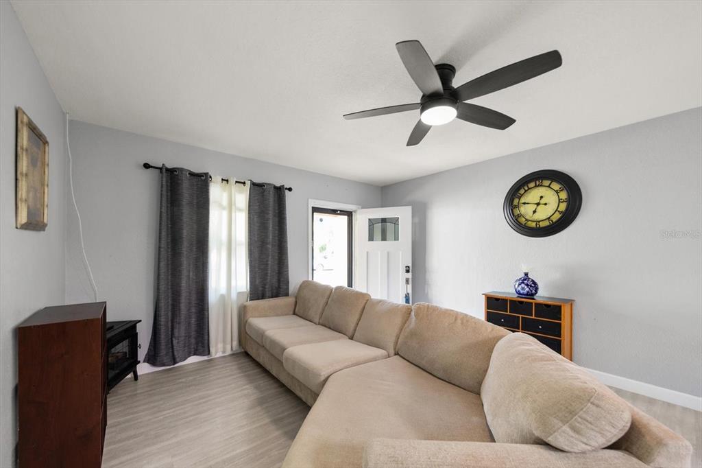 A living room features a beige sectional sofa, a ceiling fan, and a wall clock — 611 11TH STREET NW, LARGO, FL