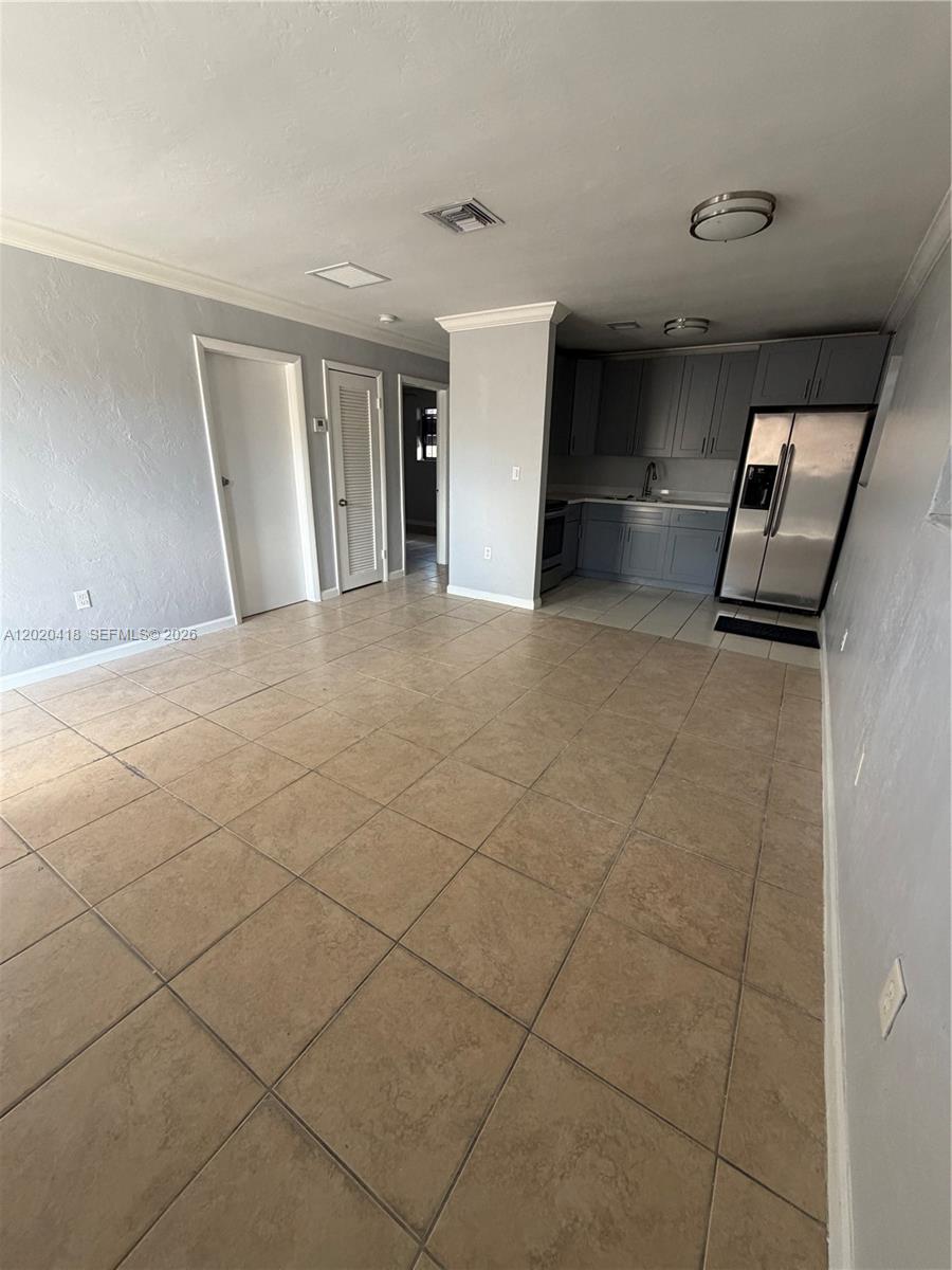 This room features light gray walls, large beige floor tiles, and a small kitchen area — 2924 NW 132nd Ter # 1, Opa-Locka FL 33054, OPA-LOCKA, FL