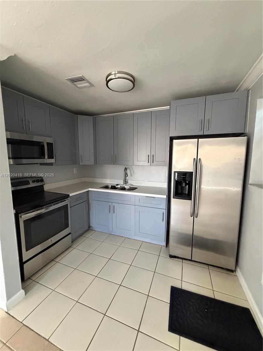 A kitchen features gray cabinets, stainless steel appliances, white countertops, and light-colored floor tiles — 2924 NW 132nd Ter # 1, Opa-Locka FL 33054, OPA-LOCKA, FL
