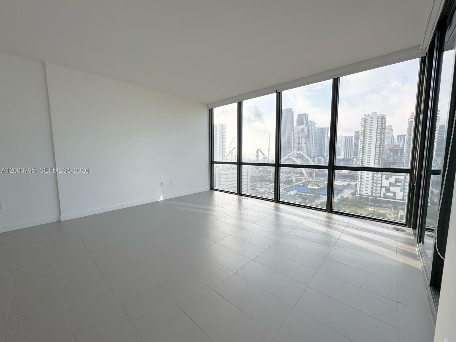 An empty room with light gray tile flooring and floor-to-ceiling windows overlooking a city skyline — 1600 NE 1st Ave # 1110, Miami FL 33132, MIAMI, FL