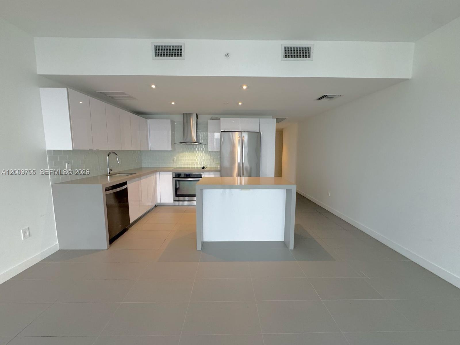 A modern kitchen features white cabinets, stainless steel appliances, and a gray waterfall island — 1600 NE 1st Ave # 1110, Miami FL 33132, MIAMI, FL