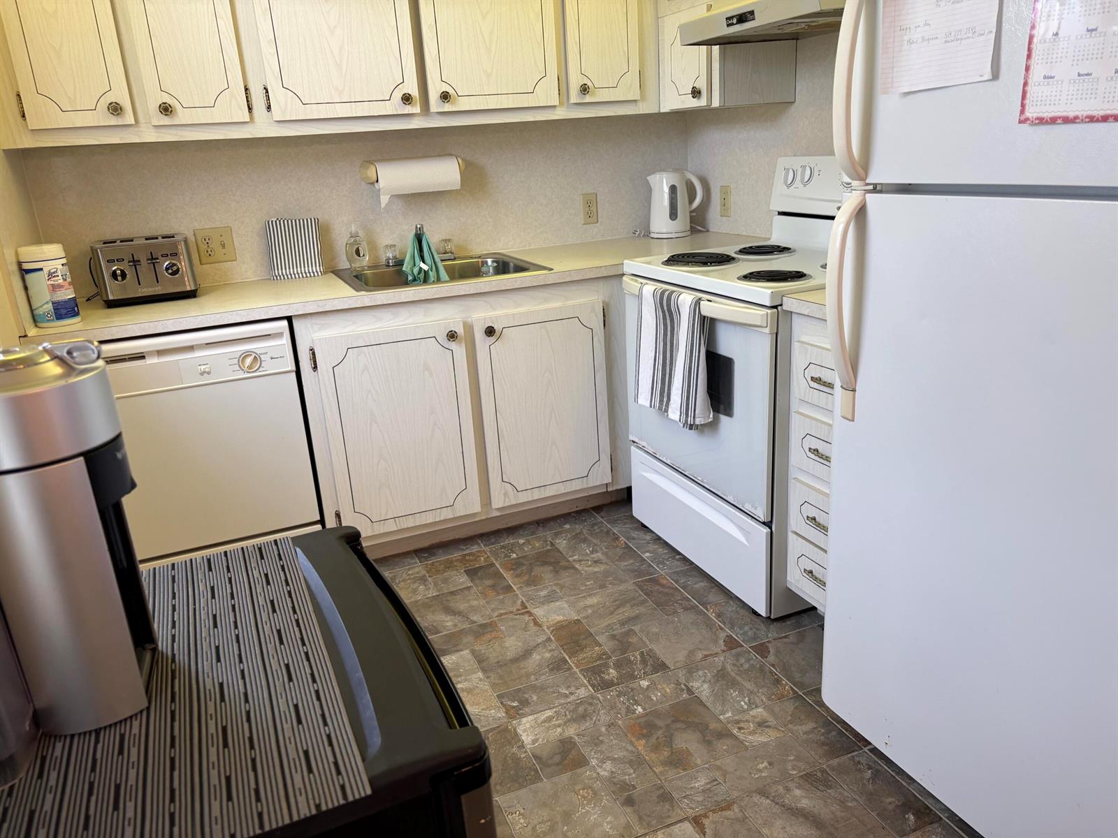 A kitchen features white cabinets, a white stove, a dishwasher, and patterned vinyl flooring — 112 C Preston Way # C, Boca Raton FL 33434, BOCA RATON, FL