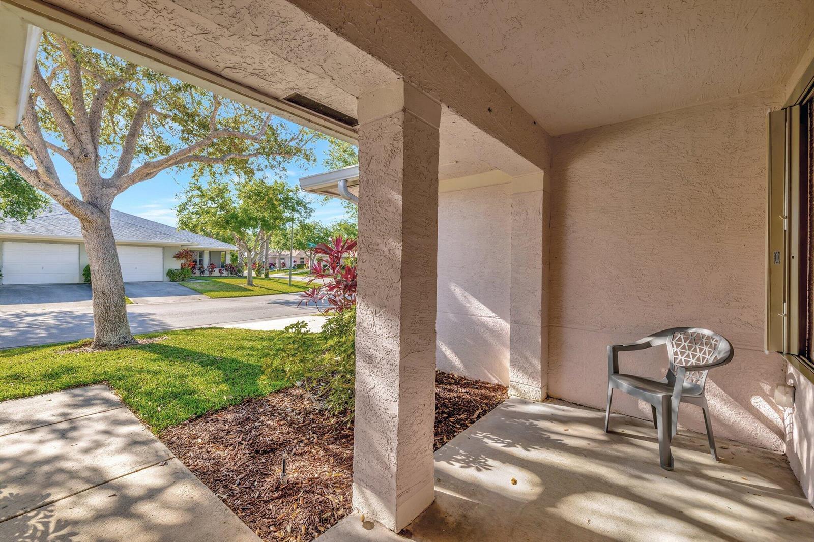 A covered concrete patio features a single gray plastic chair and a view of landscaping — 1804 E Sanderling Lane # B, Fort Pierce FL 34982, FORT PIERCE, FL