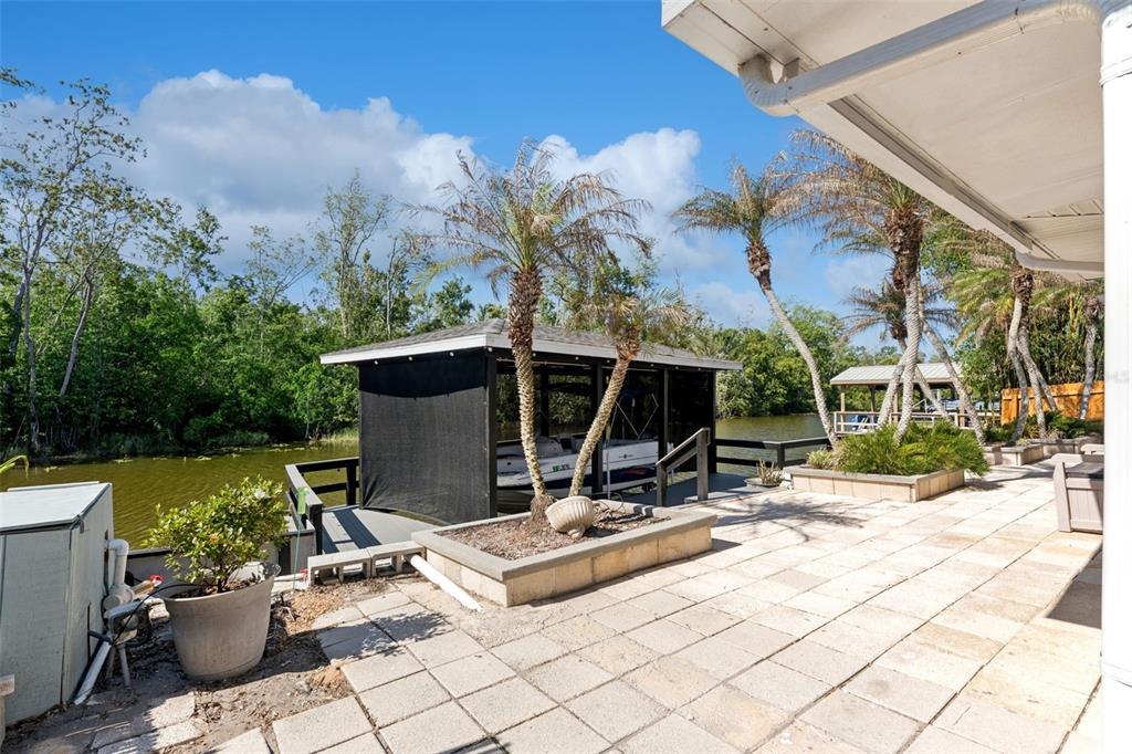 A paved patio overlooks a canal with a covered boat slip and palm trees — 13502 COUNTRY CLUB DRIVE, TAVARES, FL