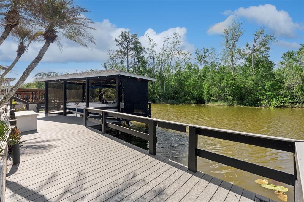 A wooden dock with a boat lift extends over a canal surrounded by lush trees — 13502 COUNTRY CLUB DRIVE, TAVARES, FL
