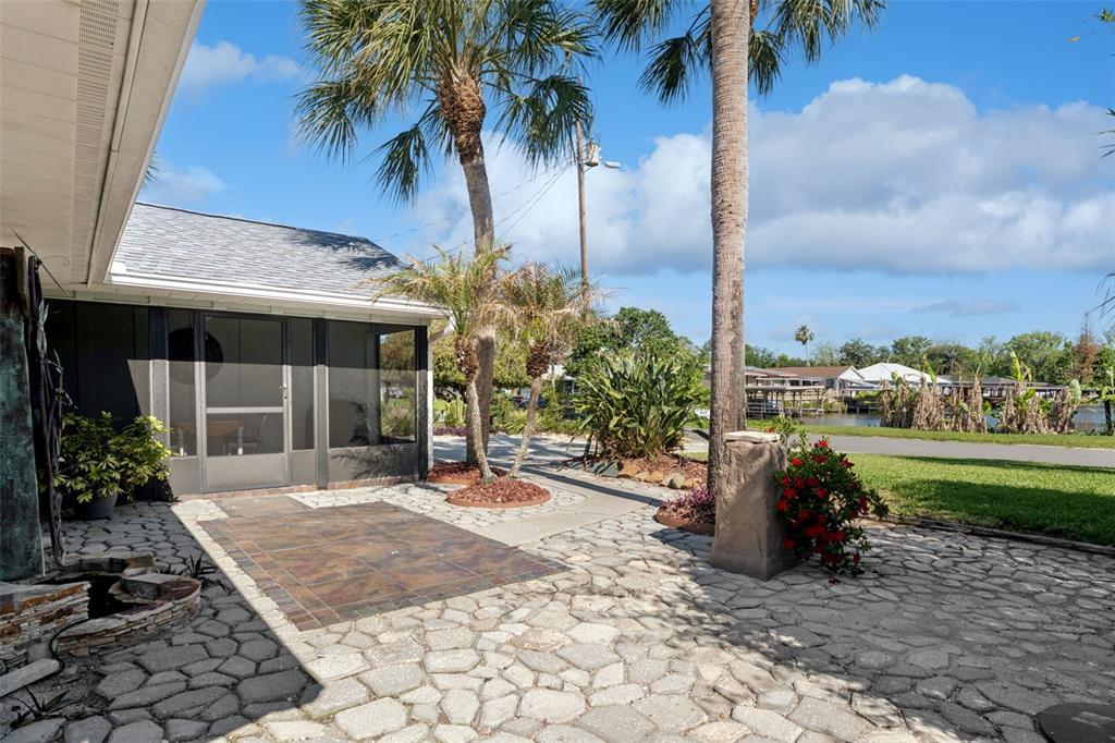 A stone patio with a tiled section leads to a screened-in porch near palm trees — 13502 COUNTRY CLUB DRIVE, TAVARES, FL