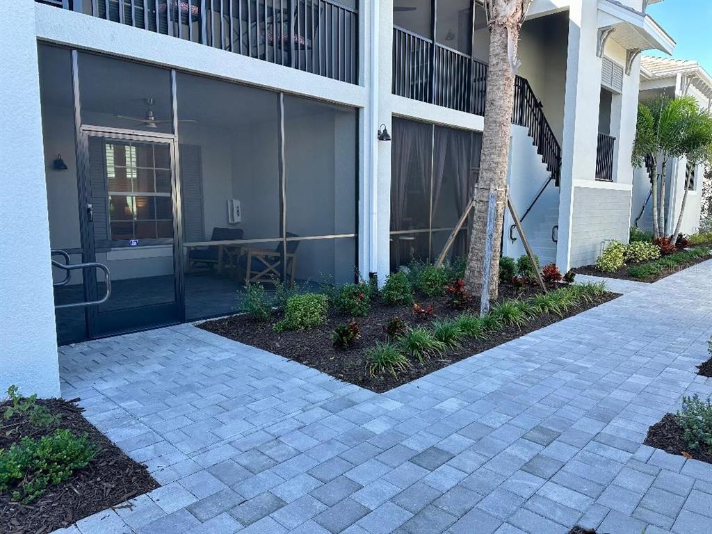 A ground-level patio with a screen enclosure sits beside a paved walkway and landscaping — 17470 OPAL SAND DRIVE UNIT 106, VENICE, FL