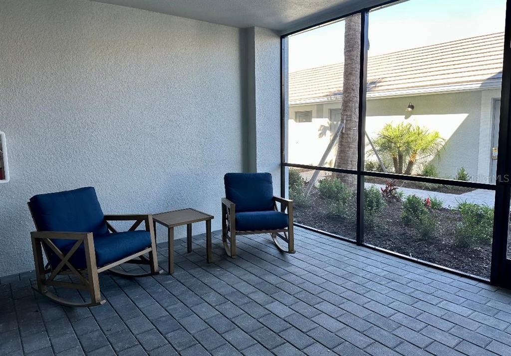 A screened-in patio features two blue rocking chairs, a small table, and paver flooring — 17470 OPAL SAND DRIVE UNIT 106, VENICE, FL