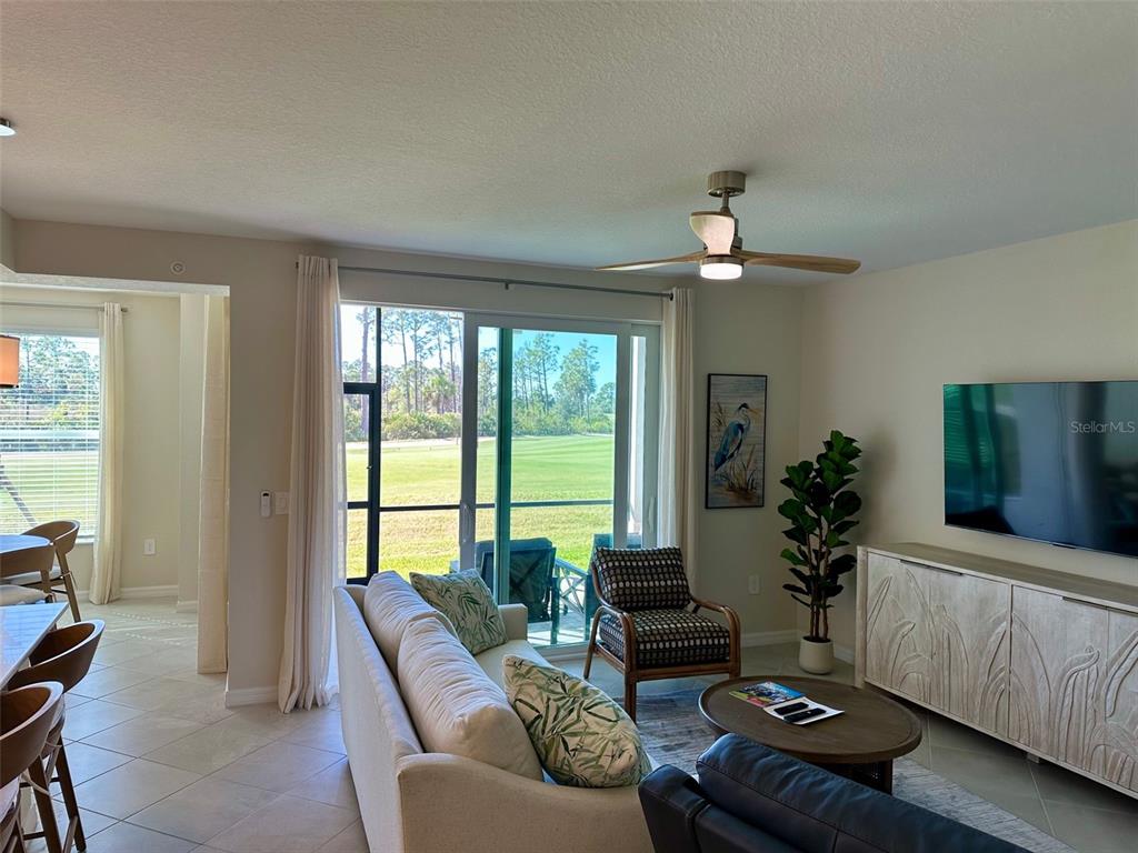 A living room features a sofa, patterned armchair, coffee table, and a view of a golf course — 17470 OPAL SAND DRIVE UNIT 106, VENICE, FL