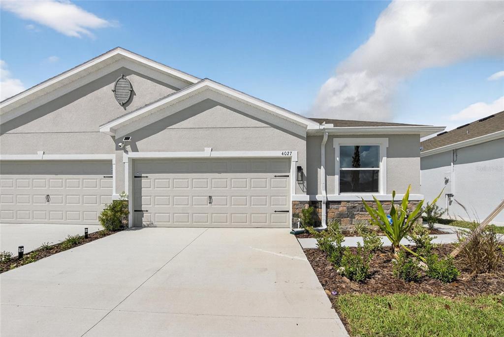 A light-colored stucco house features a two-car garage, stone accents, and a front driveway — 4027 WESTWOOD FIELDS LOOP, PLANT CITY, FL