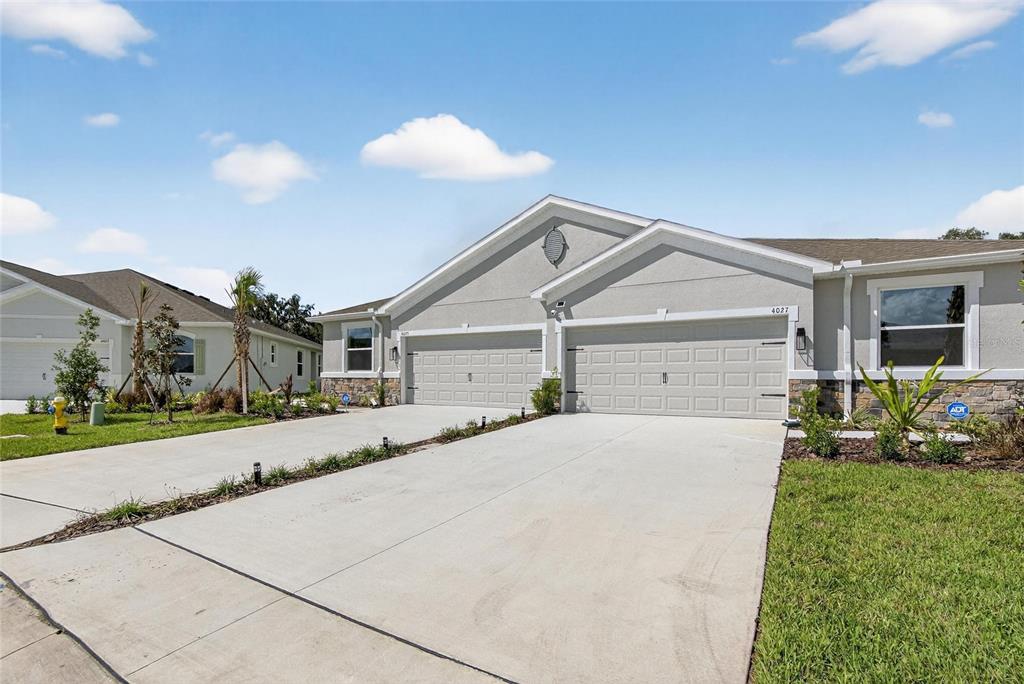 A duplex house with two garage doors and a concrete driveway under a blue sky — 4027 WESTWOOD FIELDS LOOP, PLANT CITY, FL