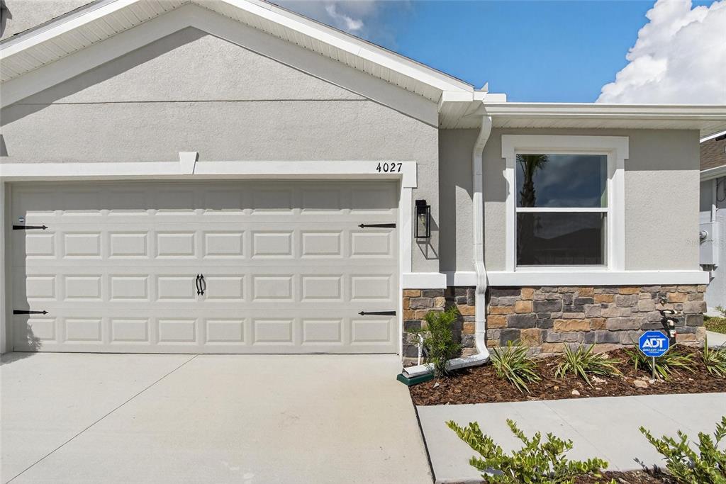 The exterior of a house features a garage, stone veneer, and a window — 4027 WESTWOOD FIELDS LOOP, PLANT CITY, FL