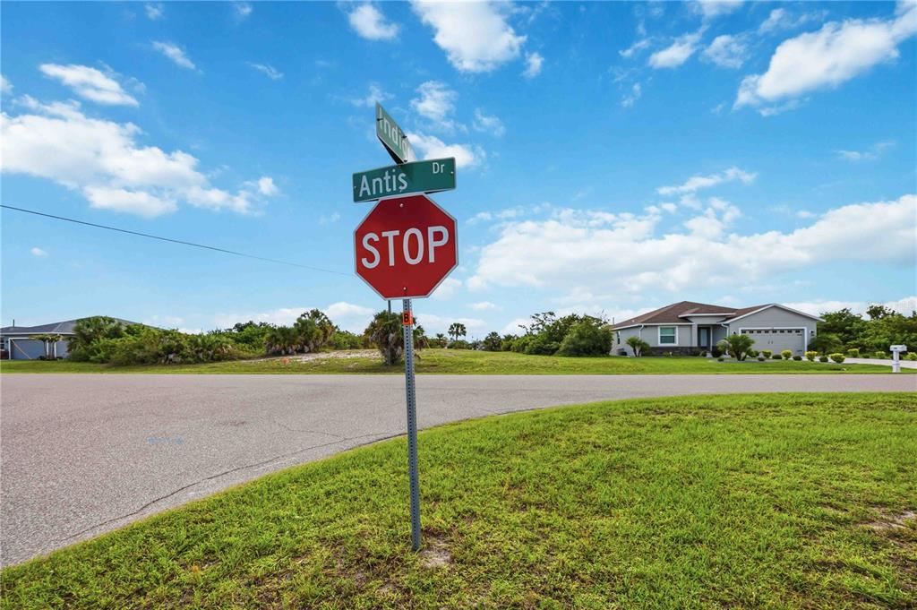 A stop sign and street name sign stand at a suburban intersection under a blue sky — 116 ANTIS DRIVE, ROTONDA WEST, FL